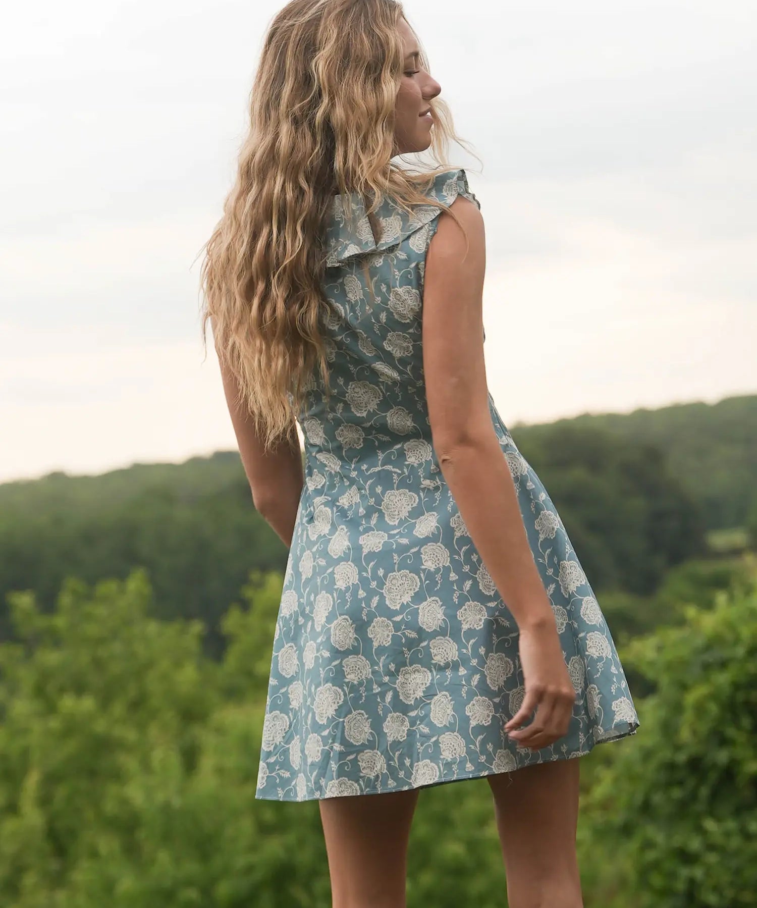 Woman in a floral dress standing outdoors with greenery in the background