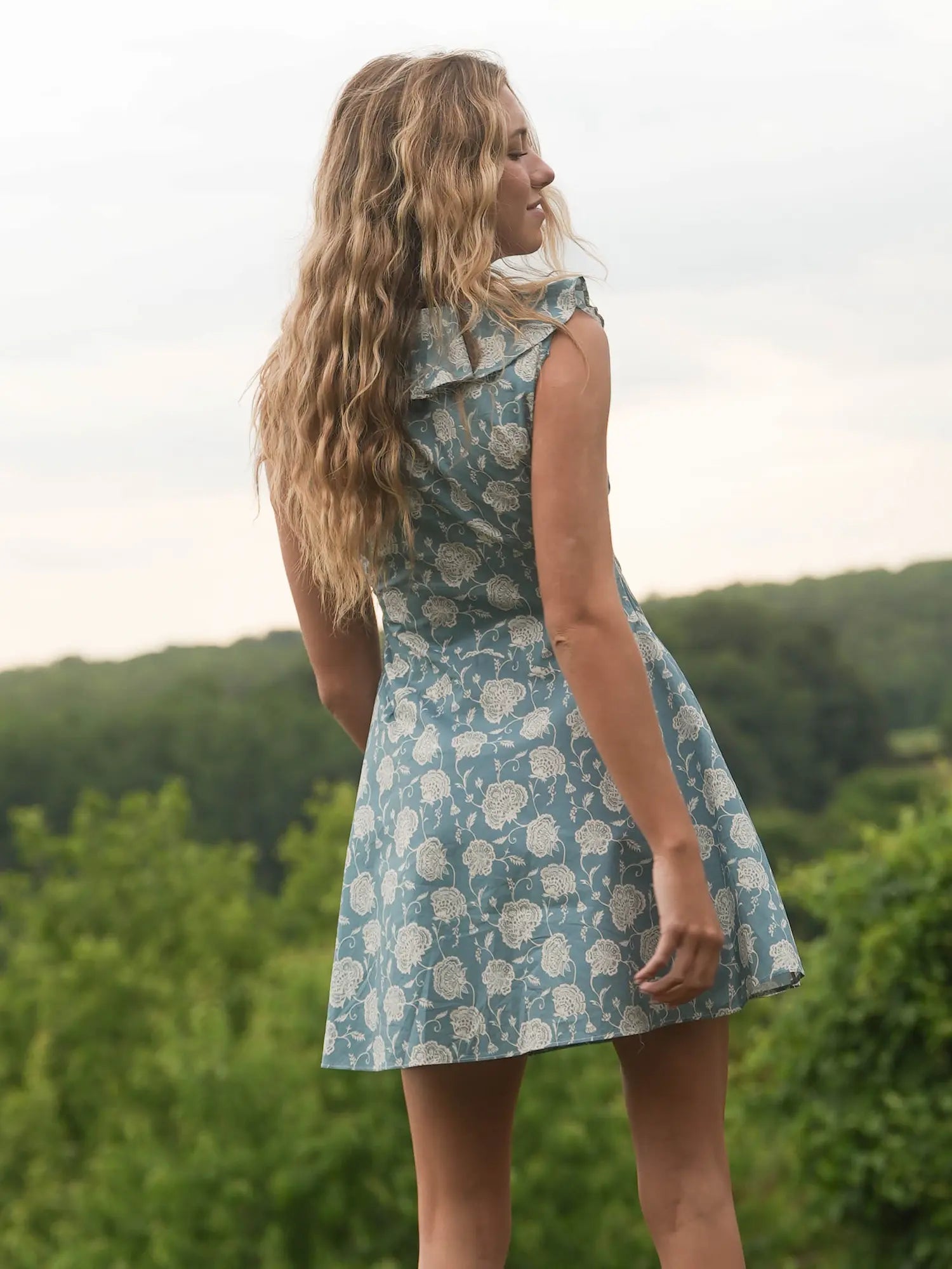 Woman in a floral dress standing outdoors with greenery in the background