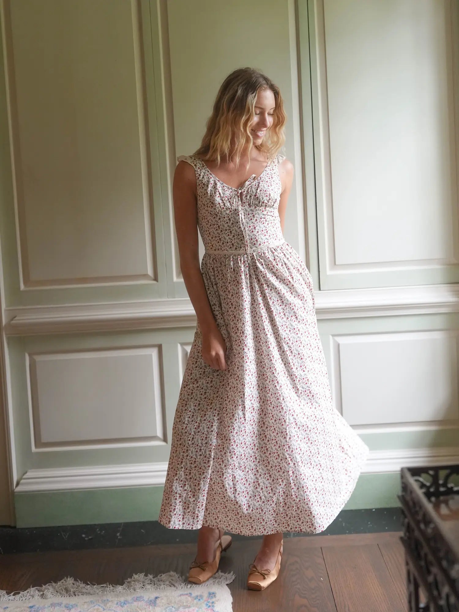 Woman wearing a floral dress standing in a room with paneled walls.