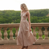 Woman in a floral dress standing on a balcony with a scenic view of trees.