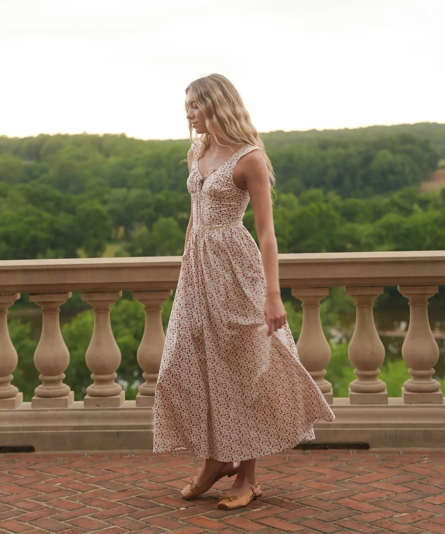 Woman in a floral dress standing on a balcony with a scenic view of trees.