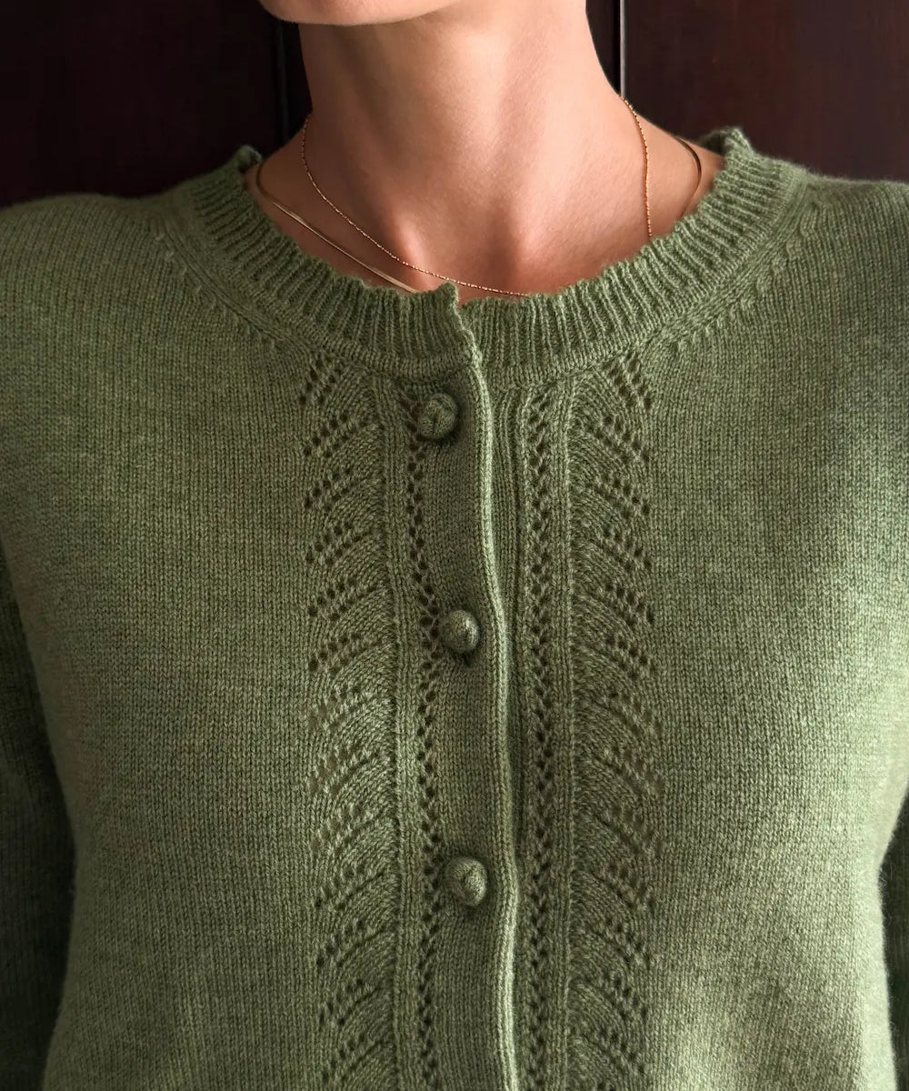 A close-up of a person wearing an olive green knitted cardigan with a button-front closure and textured knit patterns.