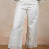 Person wearing white pants with lace trim against a plain background