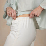 Person wearing a light gray top and white pants against a beige background