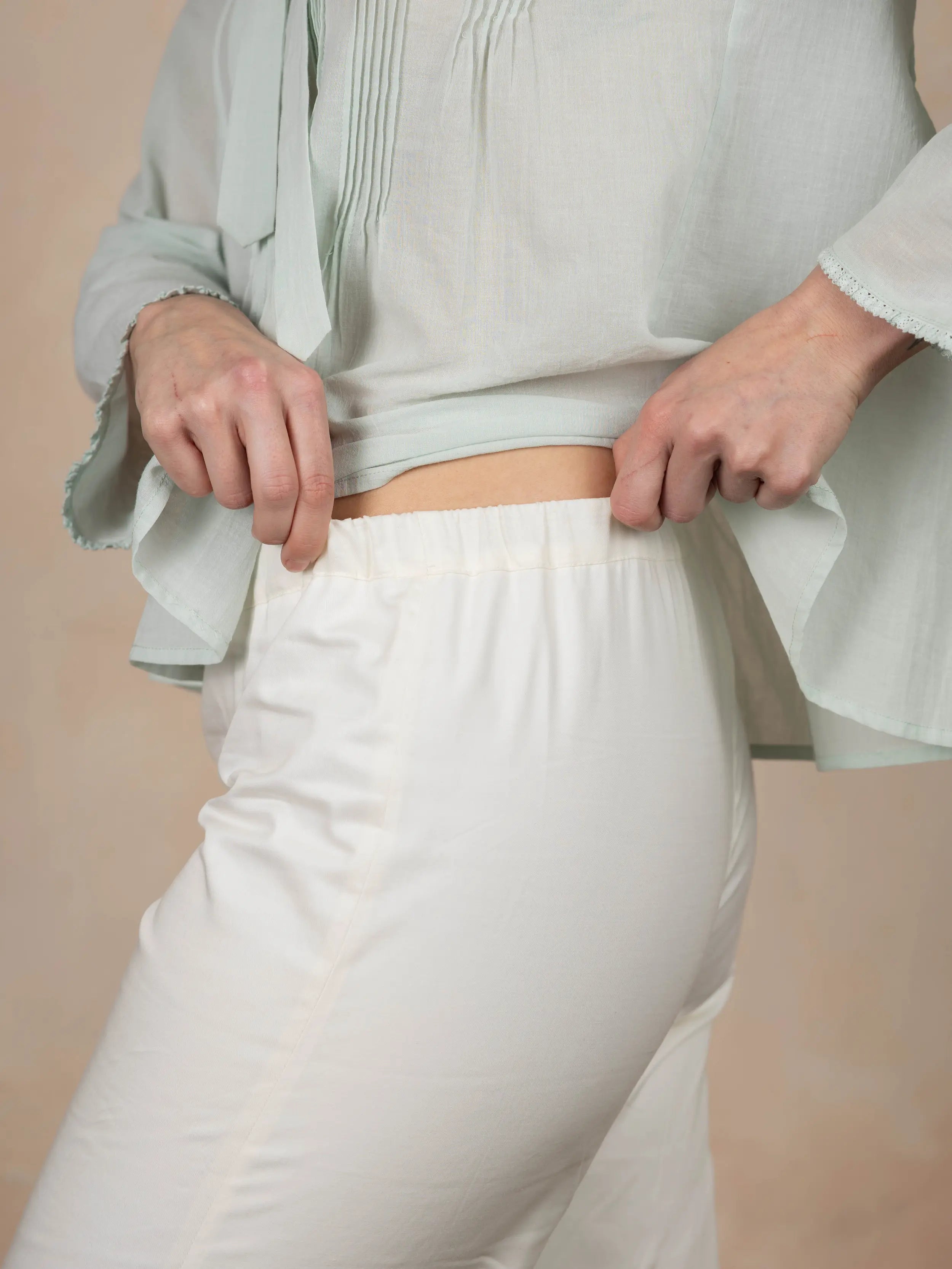 Person wearing a light gray top and white pants against a beige background