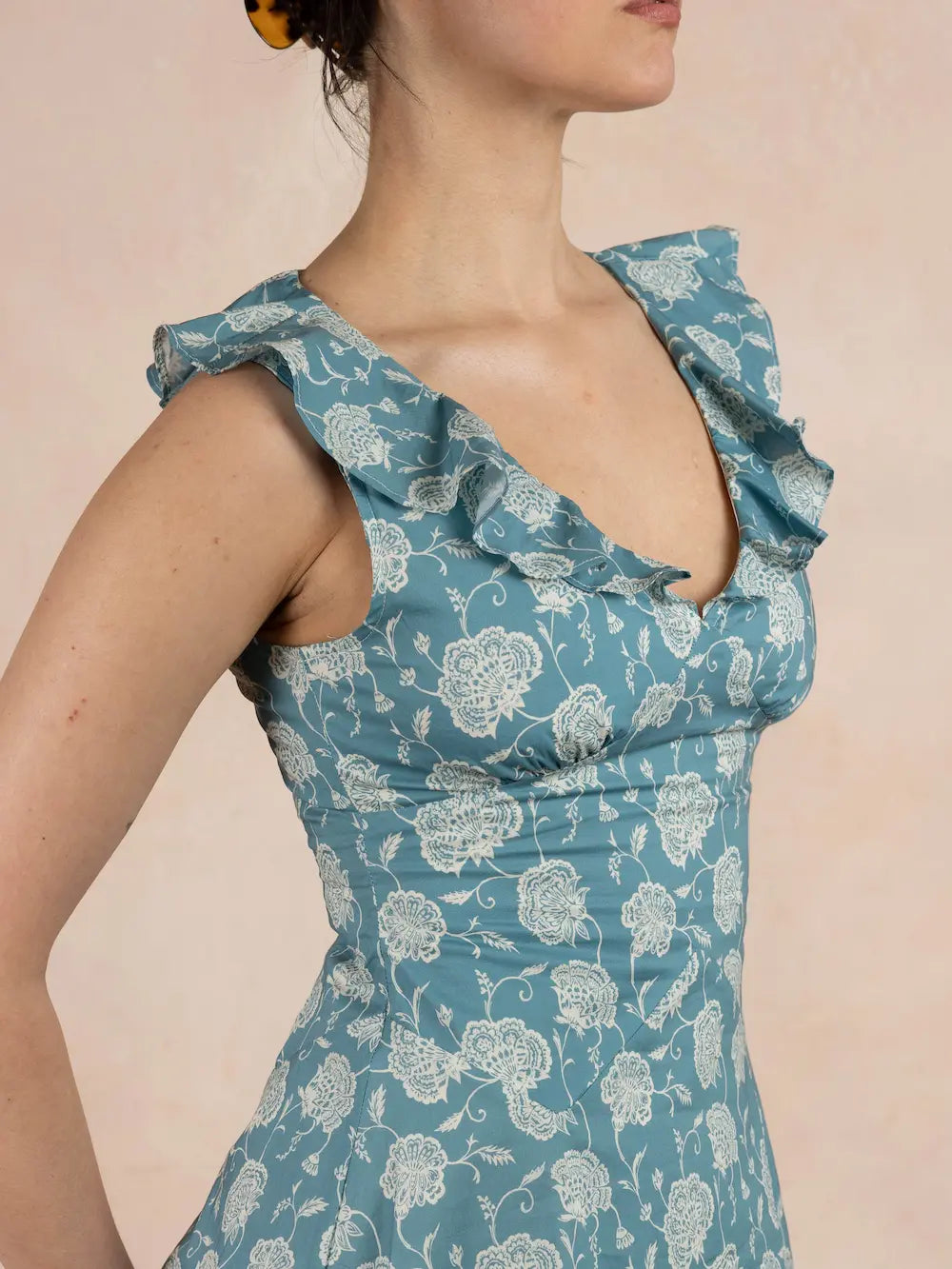 Woman wearing a blue floral dress with ruffled shoulders against a pink background