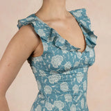 Woman wearing a blue floral dress with ruffled shoulders against a pink background