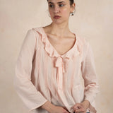 Woman wearing a light pink blouse with ruffled details against a beige background