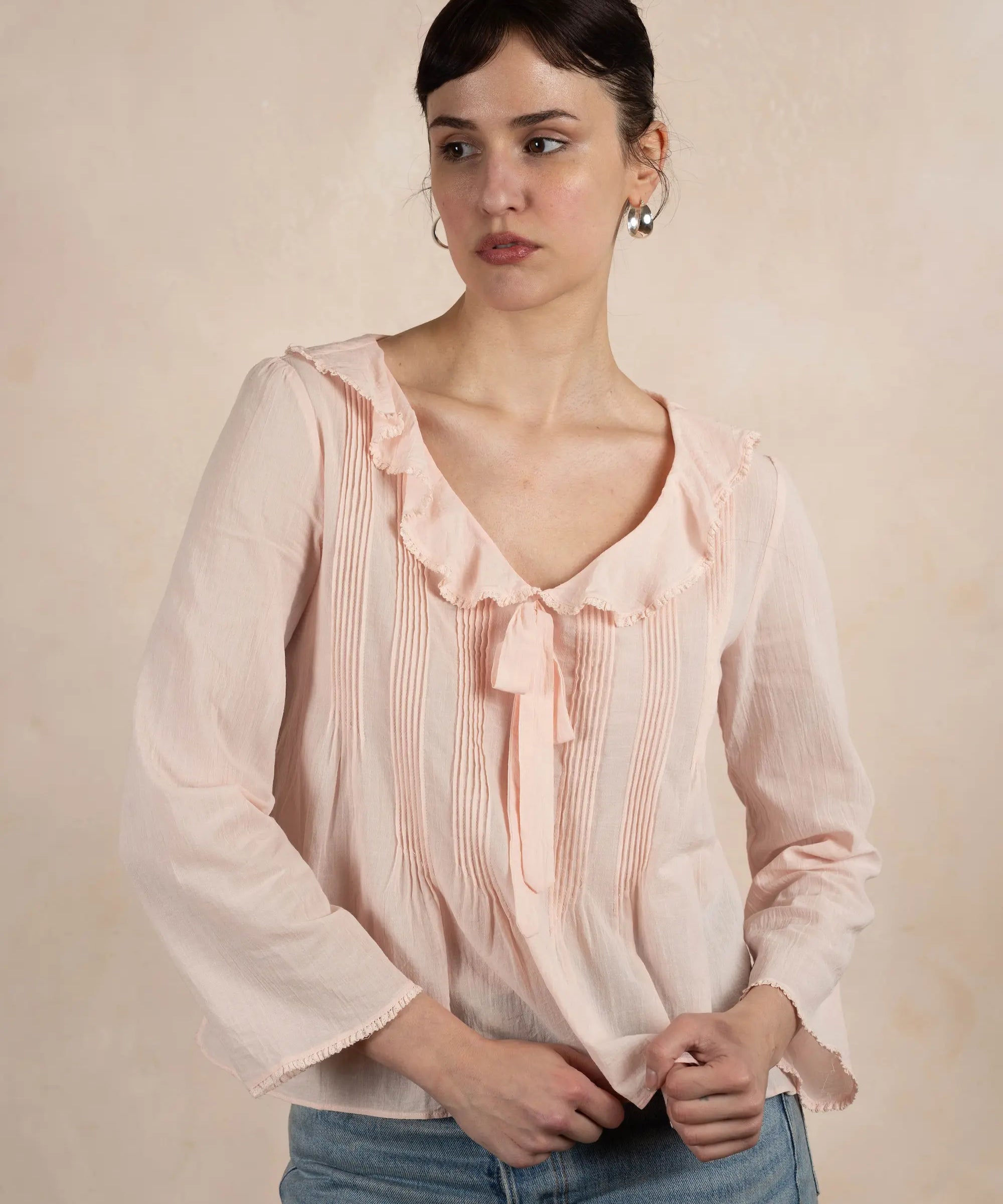 Woman wearing a light pink blouse with ruffled details against a beige background