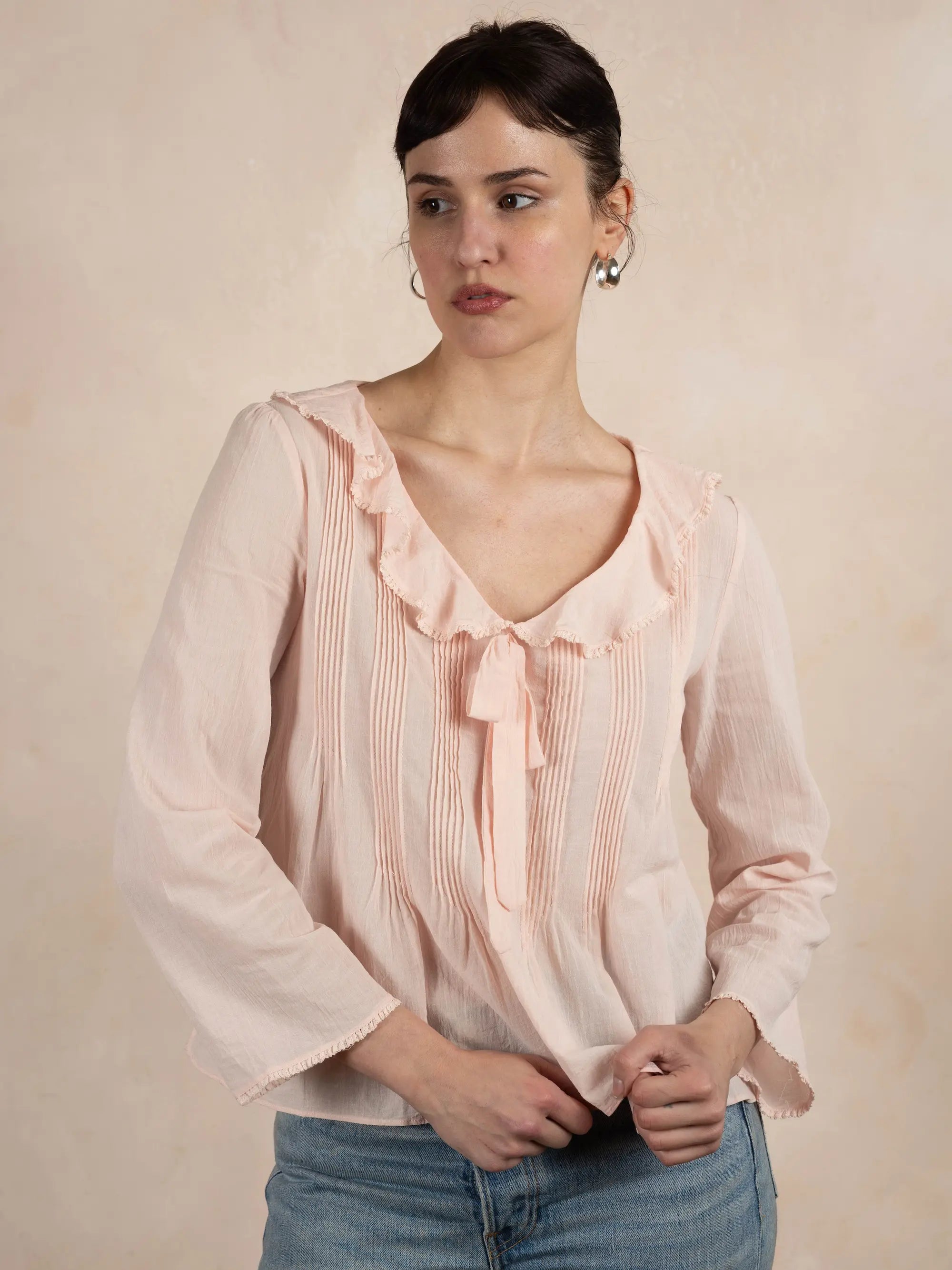 Woman wearing a light pink blouse with ruffled details against a beige background