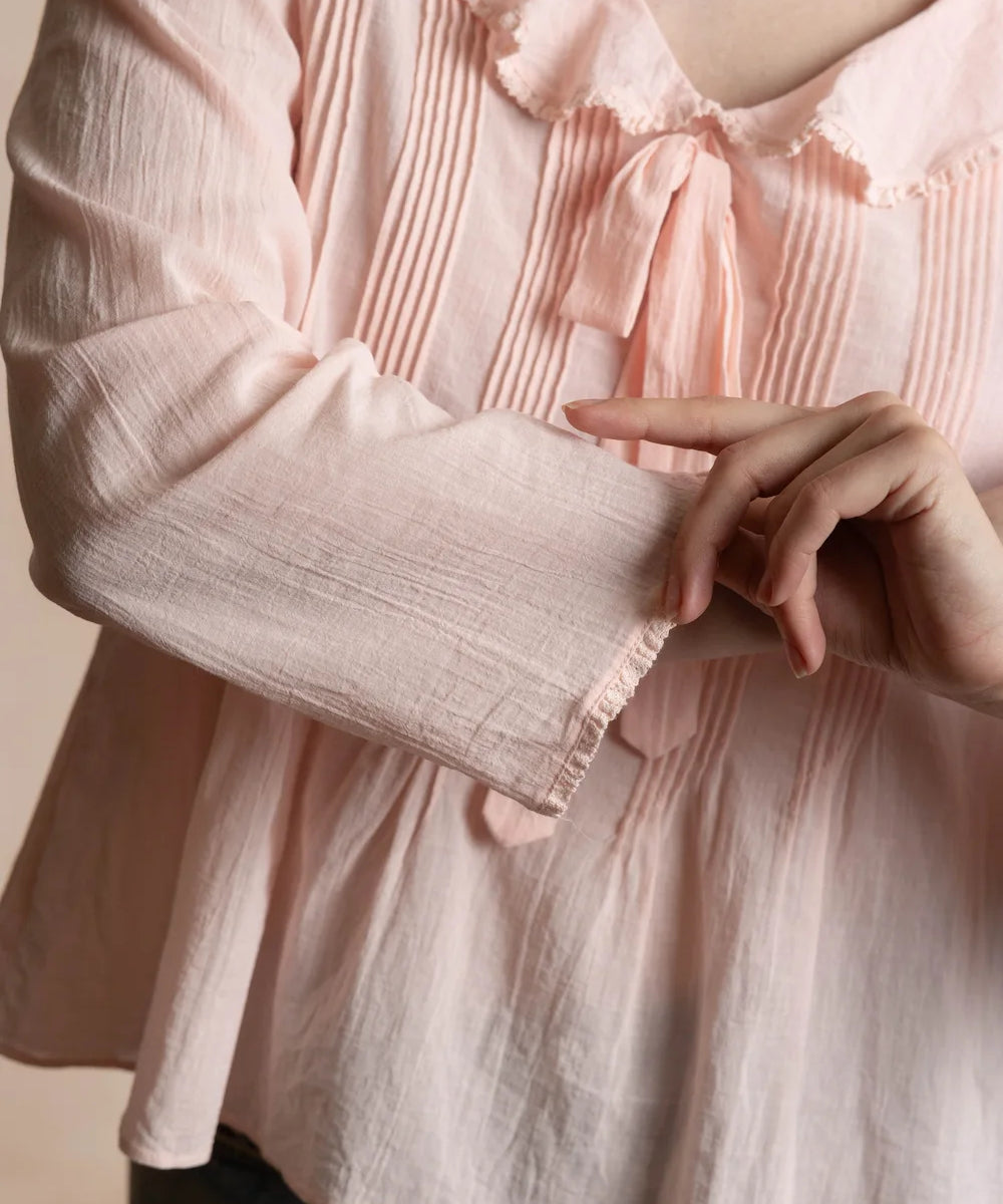 close up of a pink pintucked top with a bow