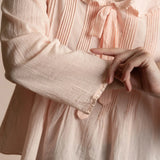 Close-up of a person wearing a light pink blouse with a bow detail.