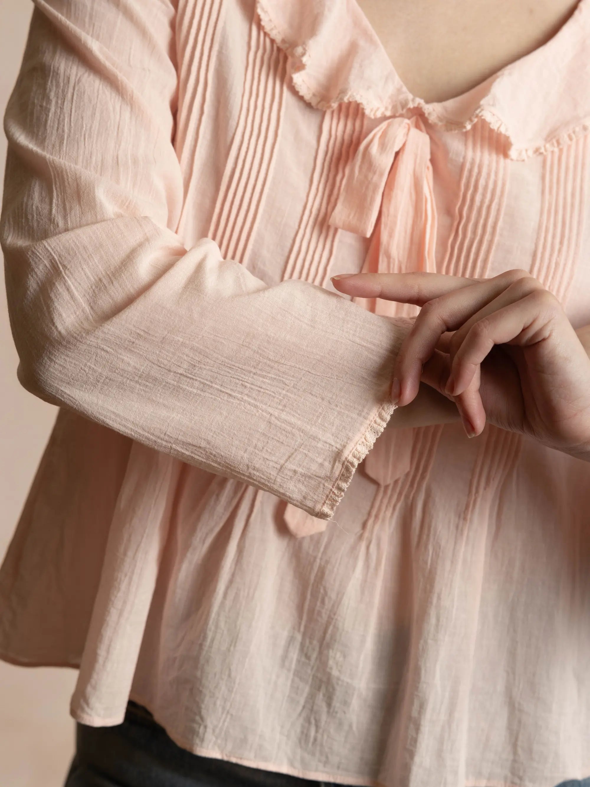 Close-up of a person wearing a light pink blouse with a bow detail.