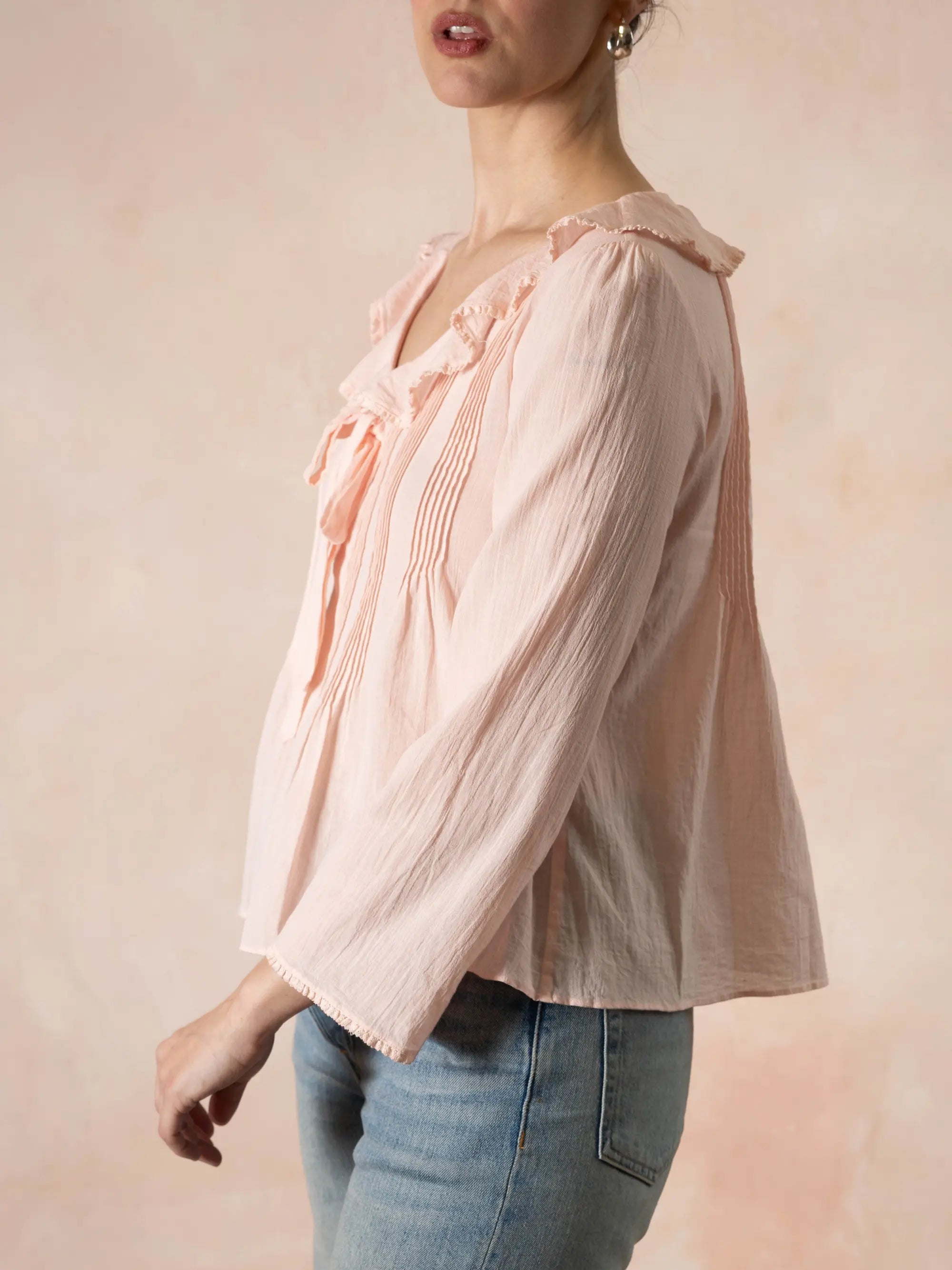 Person wearing a light pink blouse with ruffled details and blue jeans on a beige background