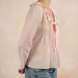 Person wearing a light pink blouse with ruffled details and blue jeans on a beige background
