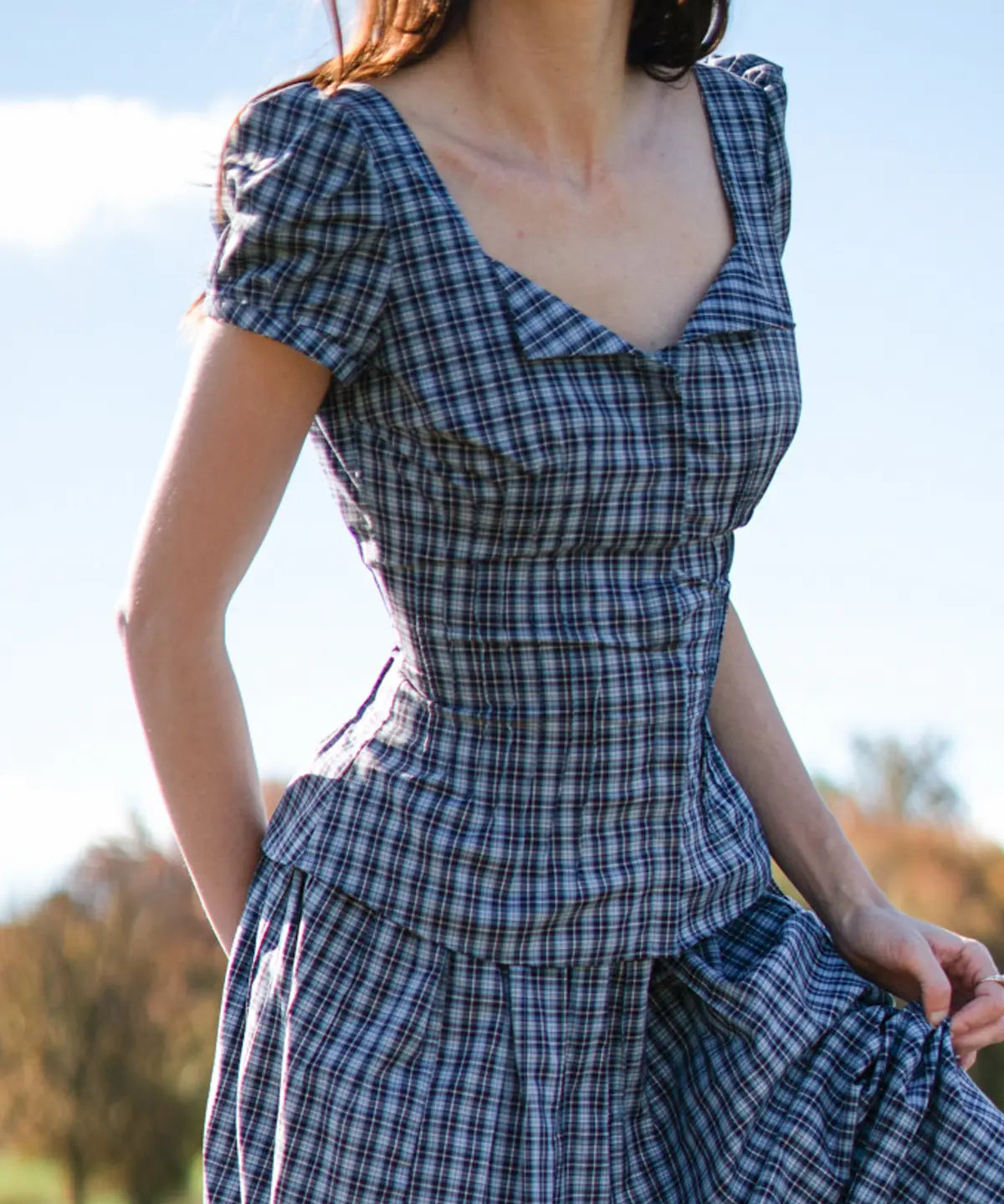 Woman wearing a blue plaid dress with a blurred natural background