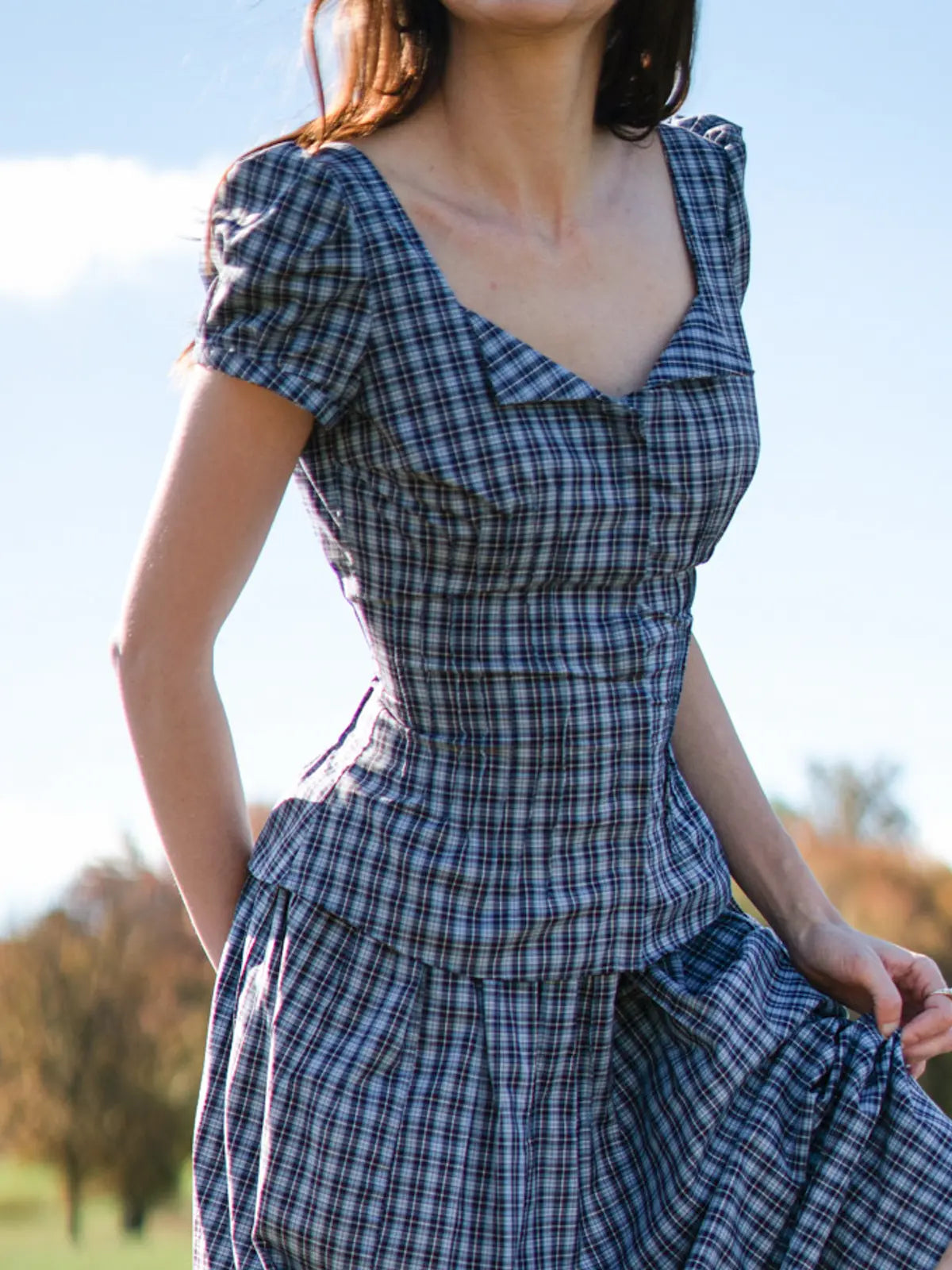 Woman wearing a blue plaid dress with a blurred natural background
