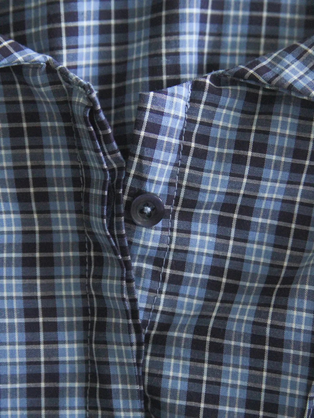 Close-up of a blue and black plaid shirt with a button.