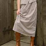 Woman wearing a brown gingham print skirt and brown boots standing against a wooden door.