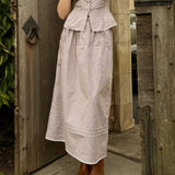 Woman wearing a brown gingham print skirt dress with a matching peplum top, standing in front of a wooden door.