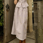 Woman wearing a light brown dress with a peplum top and skirt, standing in front of a wooden door.