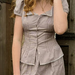 Woman wearing a checkered dress standing against a wooden background