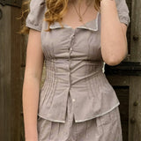 Woman wearing a checkered dress standing against a wooden background