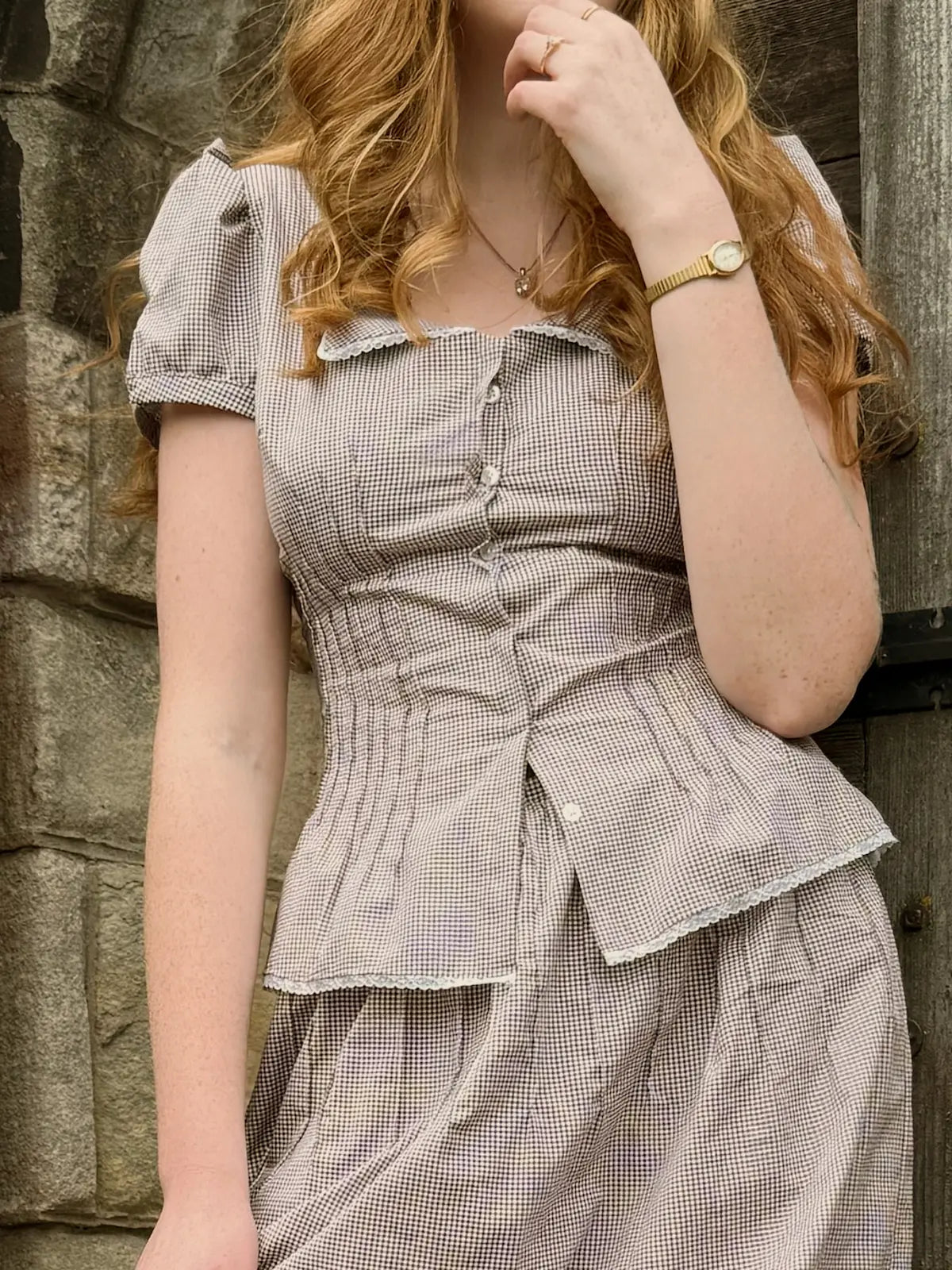 Woman wearing a checkered dress against a stone wall