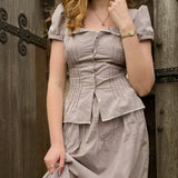 Woman wearing a gingham set standing against a wooden door.