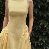 Woman wearing a yellow dress standing against a leafy green background