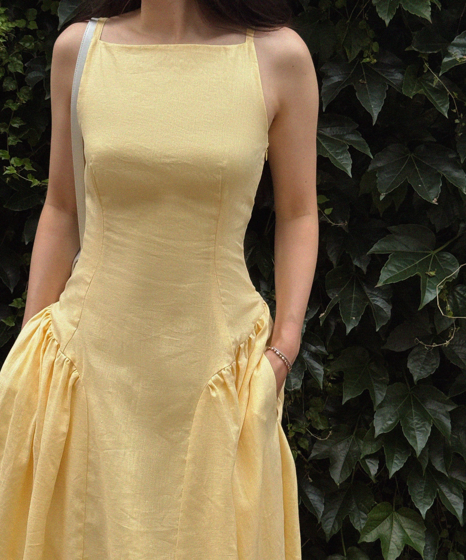 Woman wearing a yellow dress standing against a leafy green background