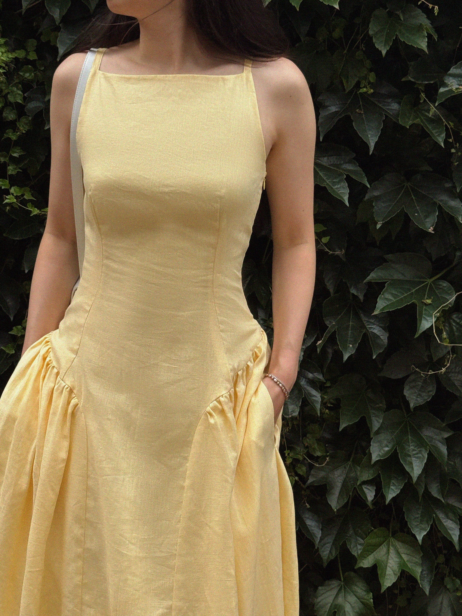Woman wearing a yellow dress standing against a leafy green background