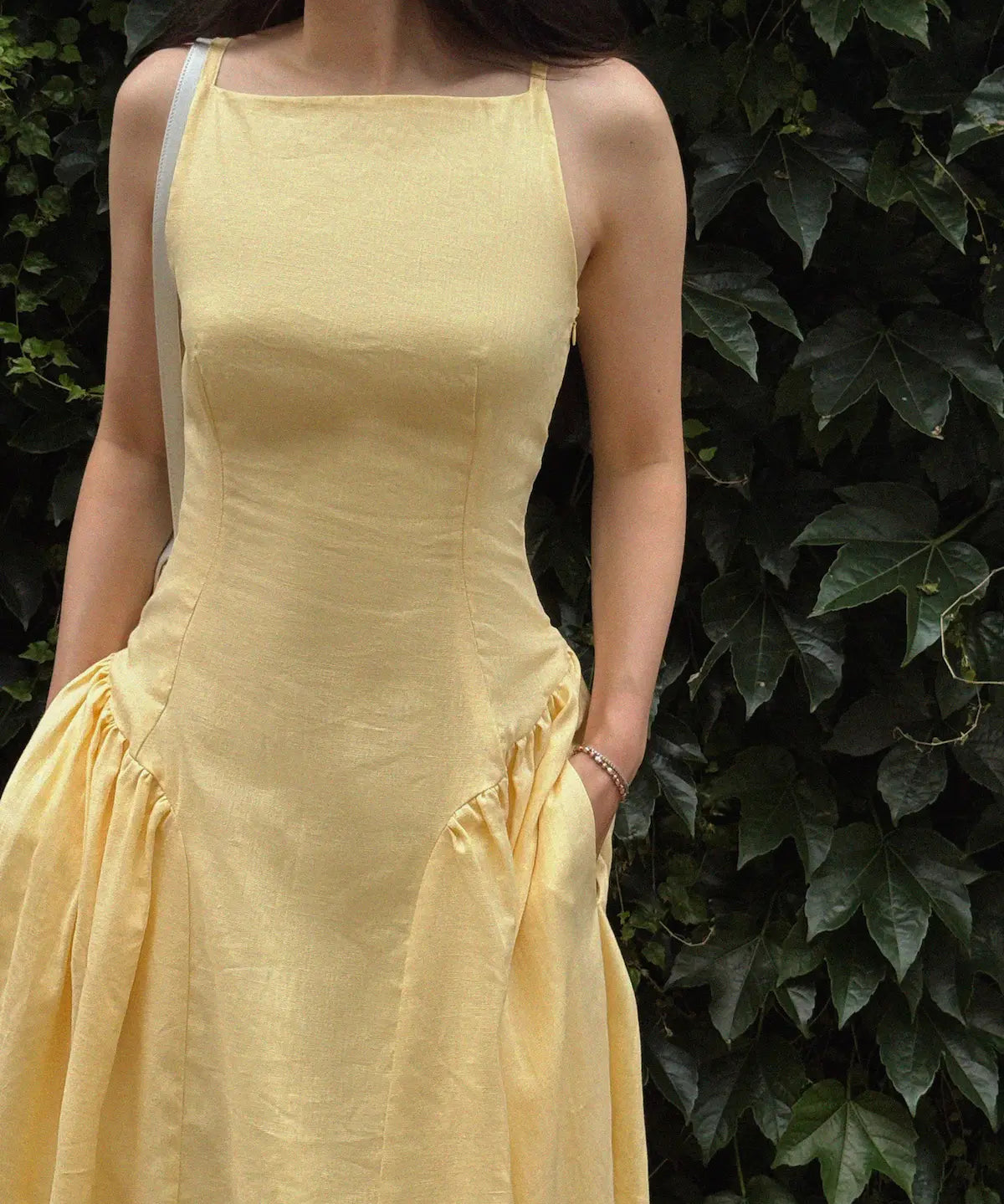 Person wearing a yellow dress standing against a green leafy background