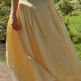 Person wearing a yellow skirt in an outdoor setting with greenery.