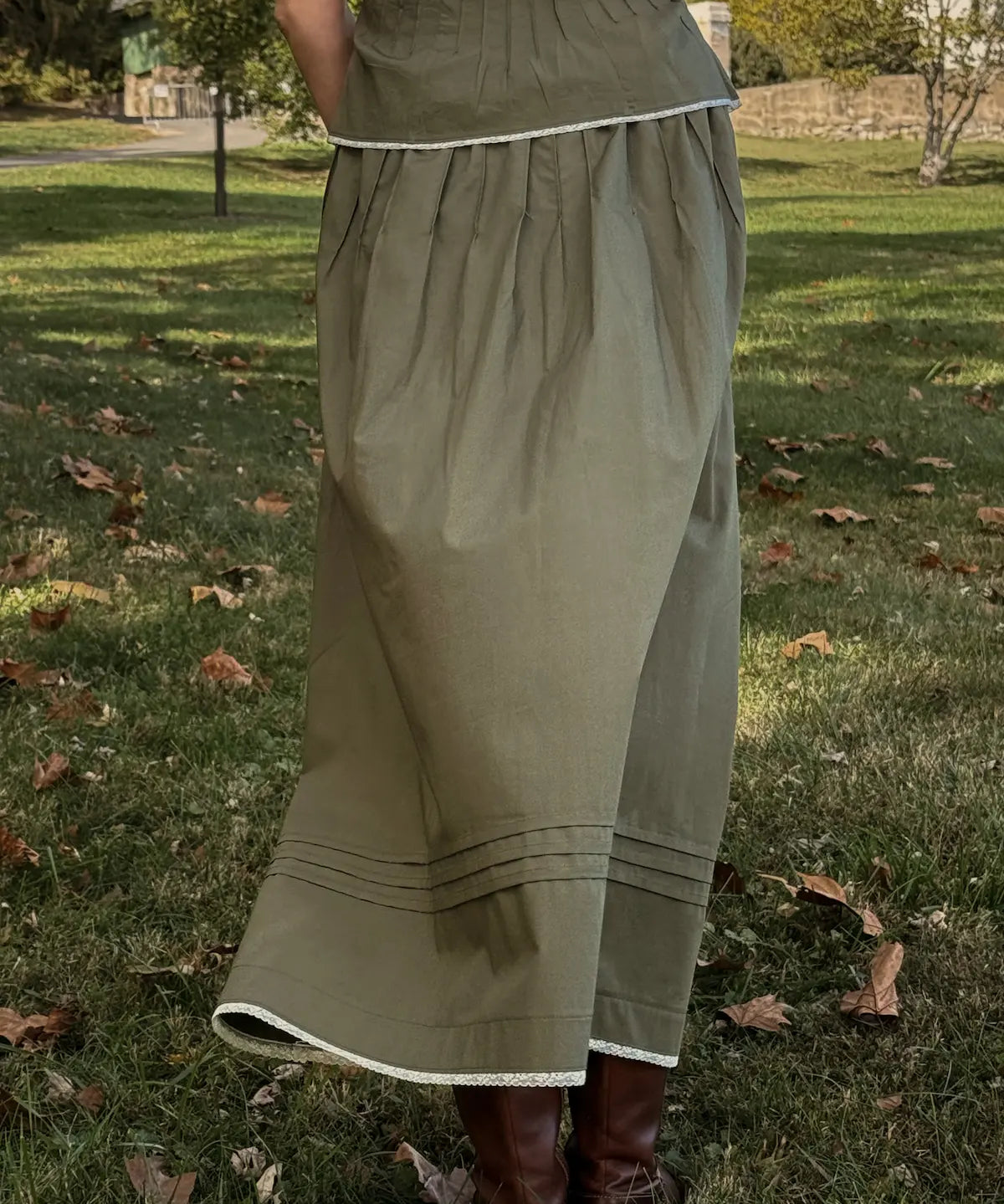 Person wearing a long green skirt standing on grass with trees in the background