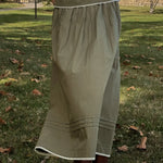 Person wearing a long green skirt standing on grass with trees in the background