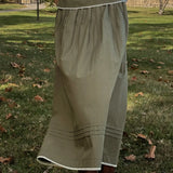 Person wearing a long green skirt standing on grass with trees in the background