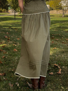 Person wearing a long green skirt standing on grass with trees in the background