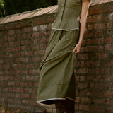 Person wearing a green set leaning against a brick wall with fallen leaves on the ground.