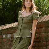Woman in a green dress leaning against a brick wall with greenery in the background