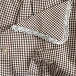 Brown and white checkered fabric with lace trim on a wooden surface