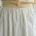 Beige sweater and white skirt with a blurred background