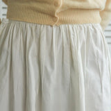 Beige sweater and white skirt with a blurred background