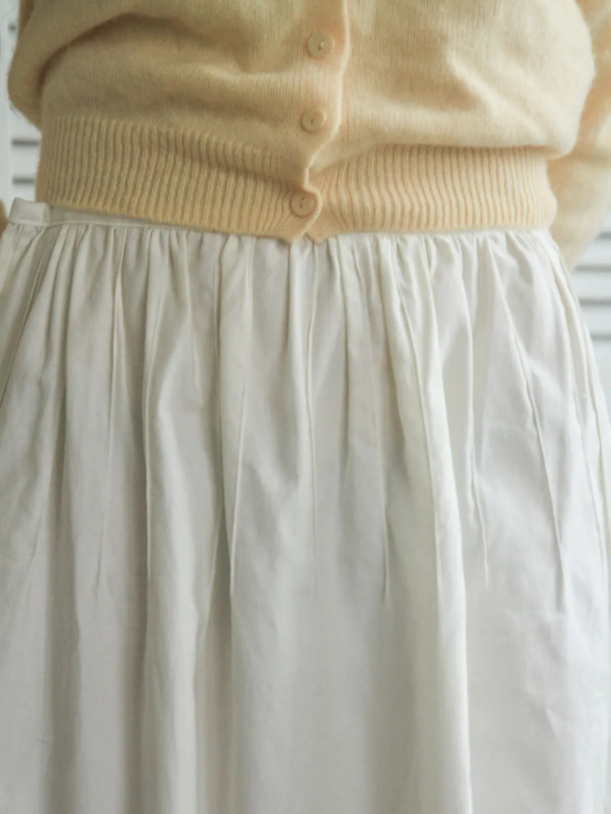 Beige sweater and white skirt with a blurred background