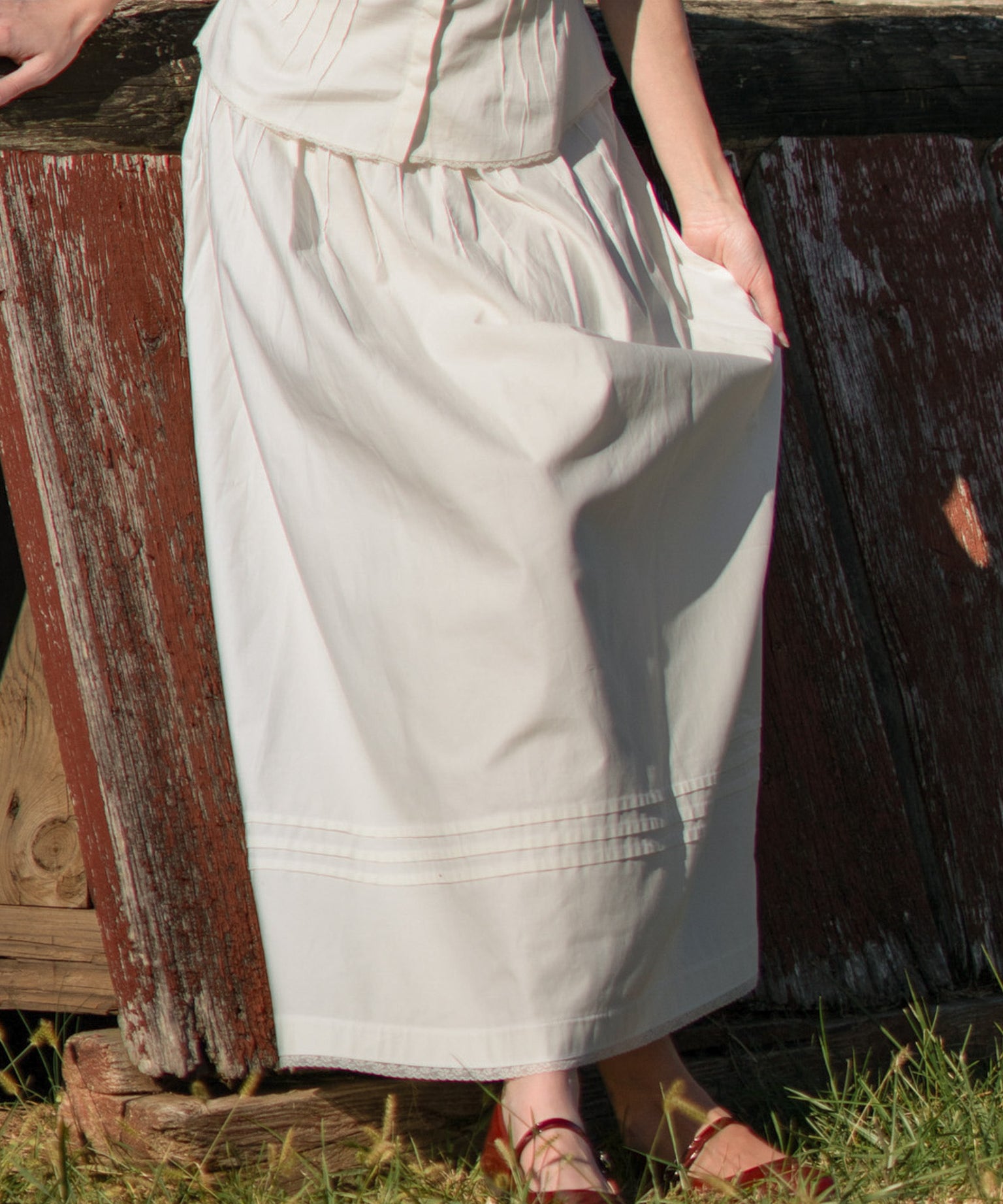 Person wearing a long light-colored skirt standing next to a wooden fence.