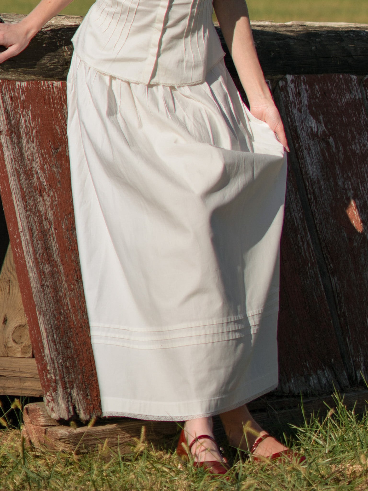 Person wearing a long light-colored skirt standing next to a wooden fence.