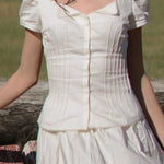 White dress with puffed sleeves worn by a person, standing against a natural background.