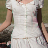 White dress with puffed sleeves worn by a person, standing against a natural background.
