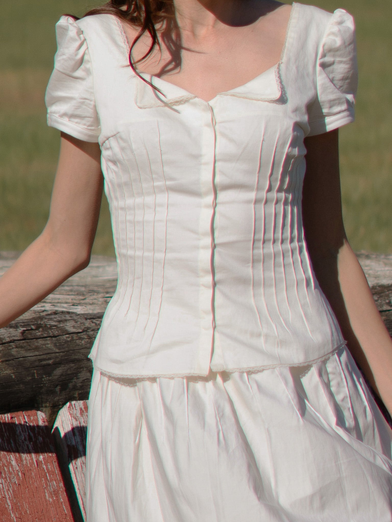 White dress with puffed sleeves worn by a person, standing against a natural background.