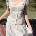 Woman wearing a white dress with puffed sleeves against a natural background